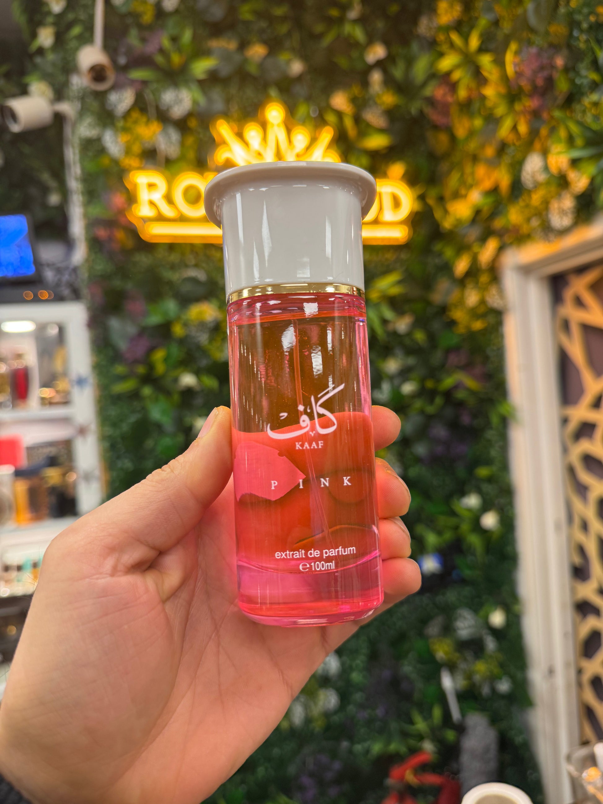 Hand holding a pink perfume bottle with a neon sign in the background
